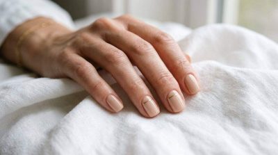 A close-up of elegant minimalist nails with soft nude polish and subtle gold line accents